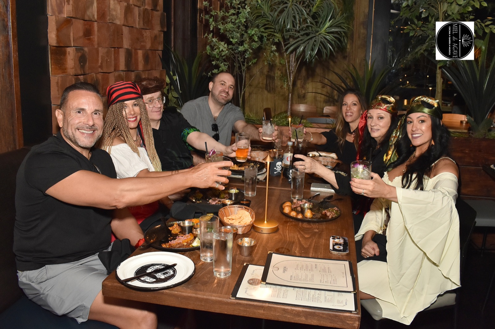 Friends in festive costumes raising drinks around a table at Miel de Agave